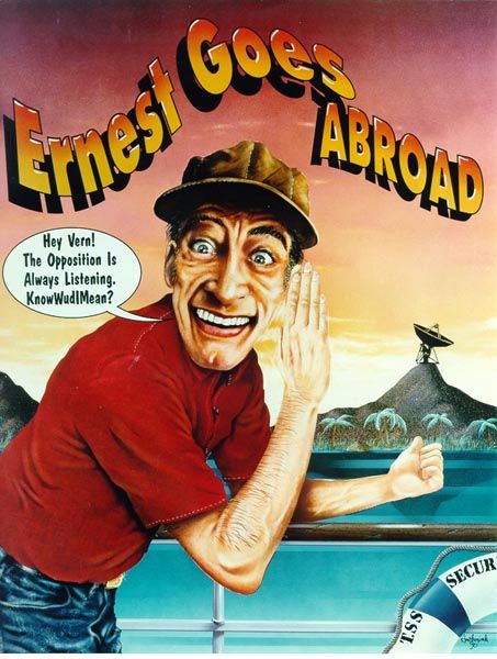 A photo of the character, Ernest, in a red shirt, whispering to the reader "Hey Vern! The Opposition is Always Listening. KnowWudIMean?" He sticks his thumb to a radio dish on a hill in the background. Above, the title "Ernest Goes Abroad"