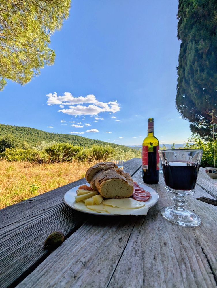 A wooden table outdoors with a plate with food, a glass and a bottle of wine 