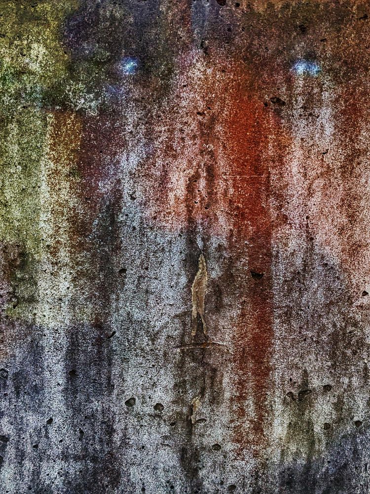 Eine graue Mauer mit grünem Grünspan auf der linken Seite und rotem Rost auf der rechten Seite.