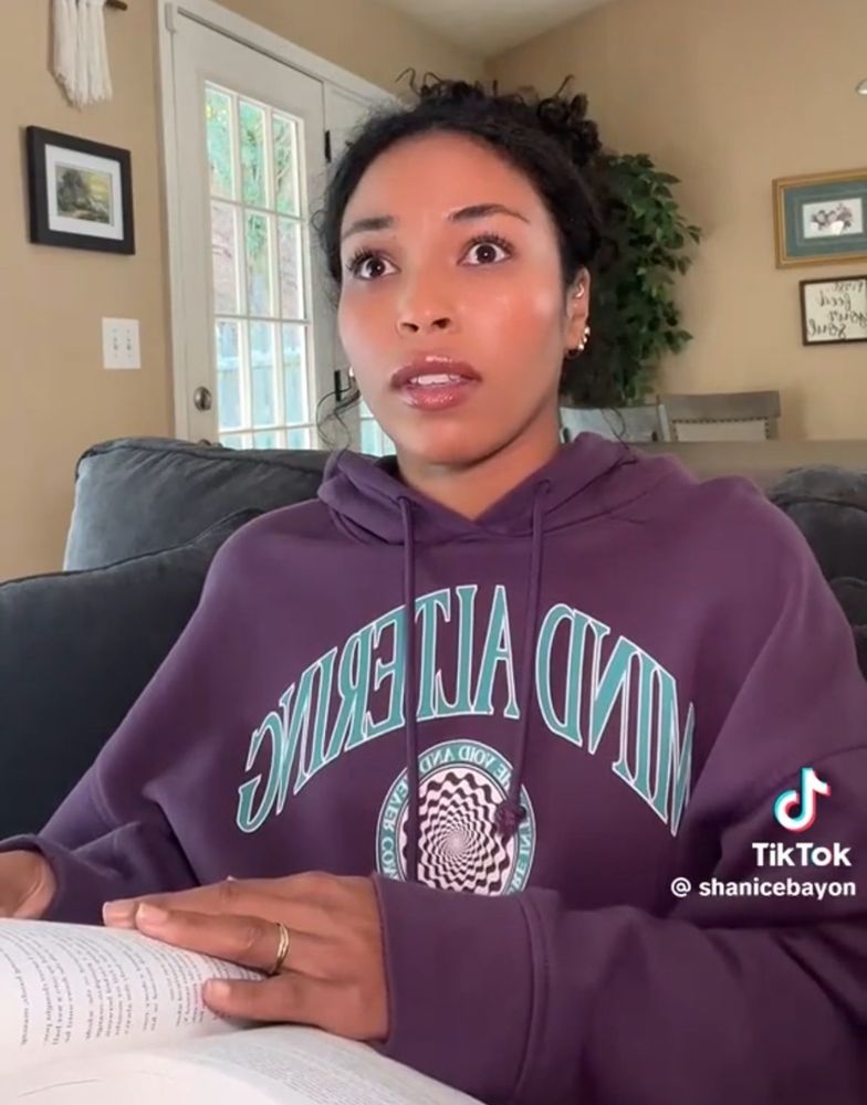 Pretty woman wearing a purple sweatshirt that reads “MIND ALTERING” on the front. She's also reading a book. Perhaps, the Bible. It doesn't matter. What matters is, she's pretty.