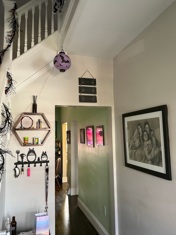Photo of a foyer with stairs to the left and a hallway leading back. Above the doorway leading to the hallway is a sign with three slate sections. 