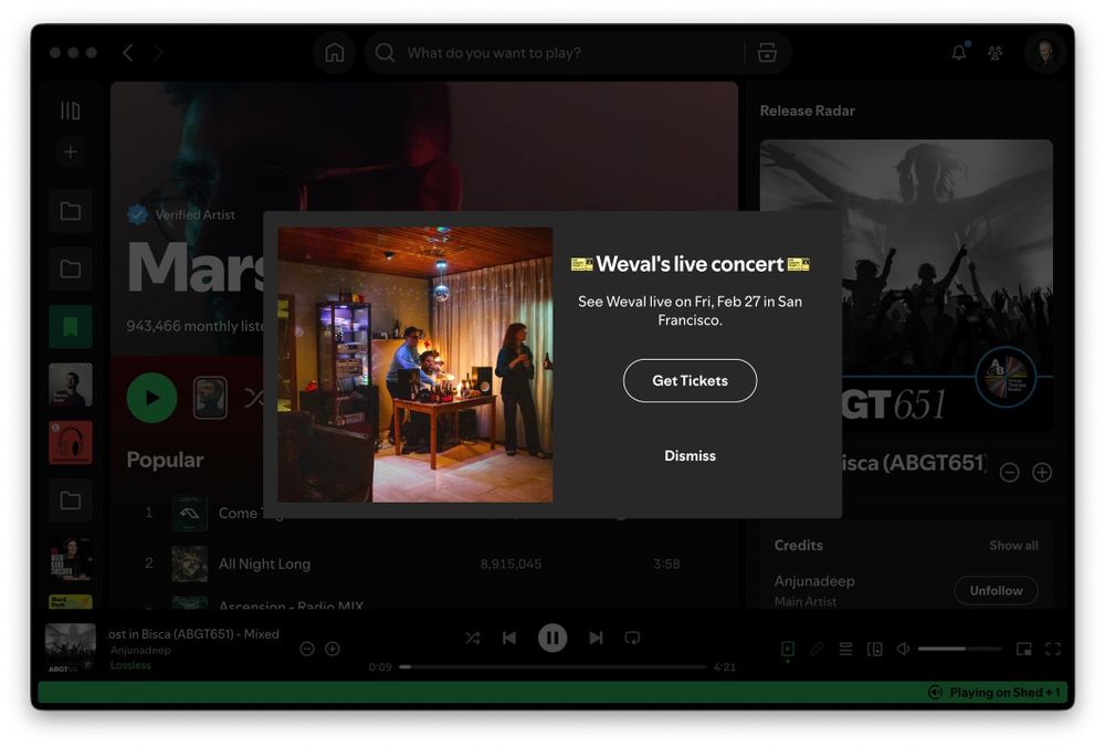 This image shows a music streaming or media playback application interface on a computer screen. A pop-up window in the center displays a concert photo with a message about Weval's live concert in San Francisco on February 27, with options to "Get Tickets" or dismiss the message. The main background has a dark theme, showing a playlist with song titles, artist names, and playback controls across the bottom. There’s a green status bar indicating the song is playing on a device named "Shed +1." The interface includes various icons for controls, settings, and navigation, with some text and elements slightly obscured by the pop-up.