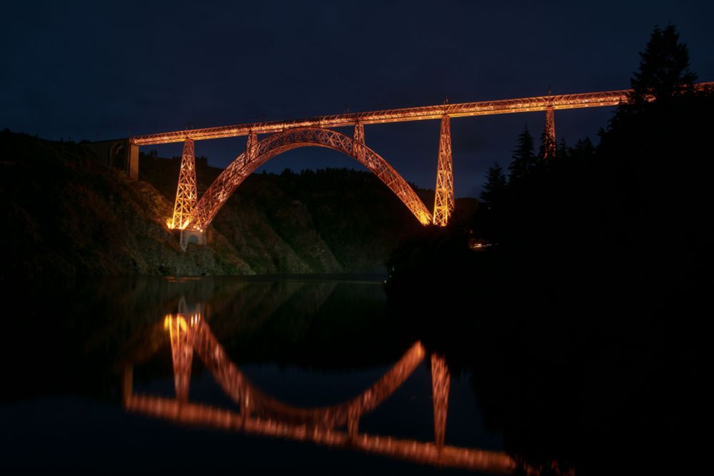 Le viaduc de Garabit éclairé de nuit.
se reflette dans la rivière de la Truyère en bas de la photo
