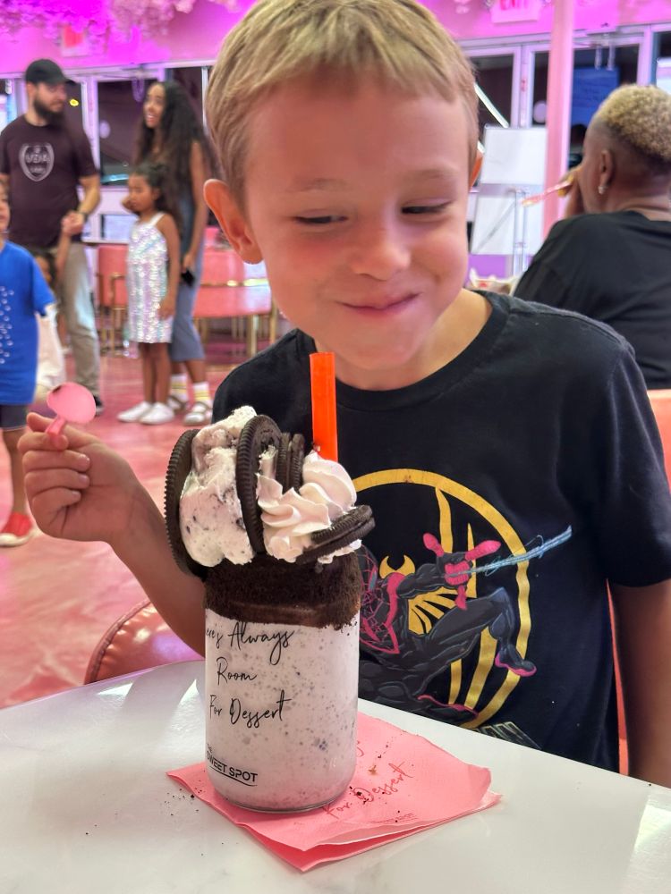 A child smirks at a cookies and cream milkshake tooped with an oreo ice cream sandwich, whipped cream, and more oreos