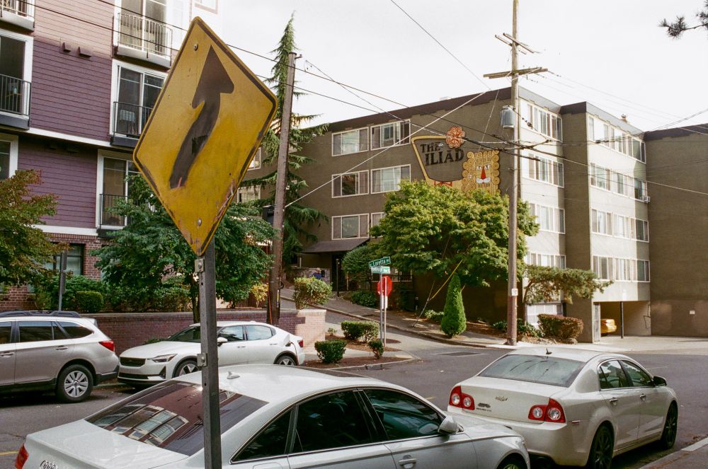 a hand-painted curve warning sign in front of a 60s apartment building with a strange drawing of a lion. building name: the iliad