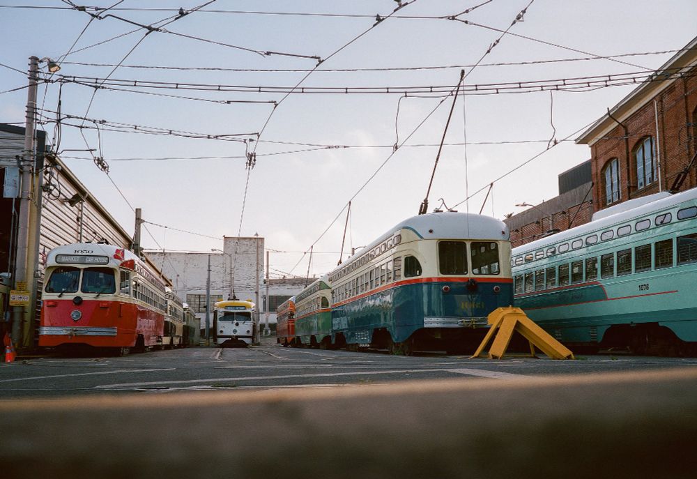 colorful streetcars sit parked in a storage yard of the S.F. Municipal Railway at sunset.