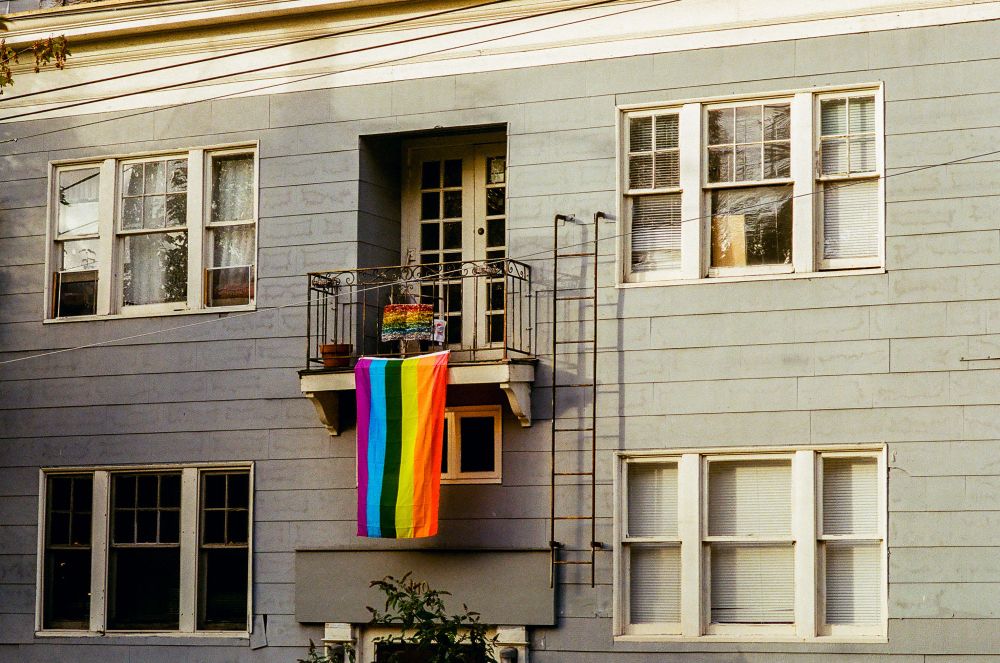 An apartment with a strange ladder to nowhere and a gay pride flag hanging off the balcony. 