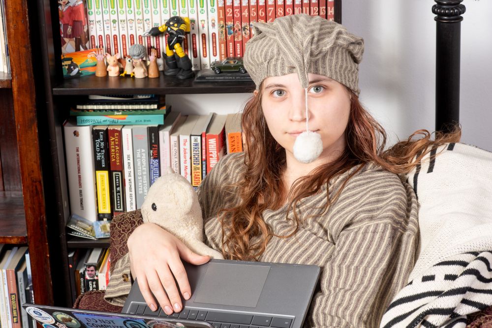 my wife on her laptop, with the poofy hat floof in front of her face