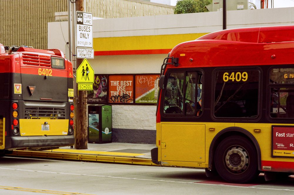 two red-and-yellow rapidride buses sit in front of a yellow-and-red Shell station