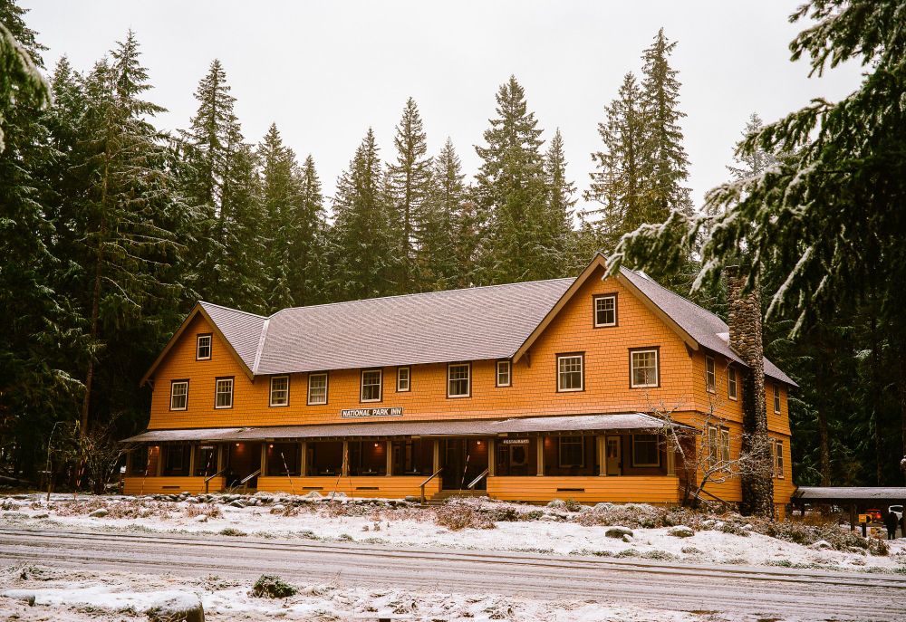 a large historic-looking hotel labeled NATIONAL PARK INN on a snowy, cloudy day, surrounded by massive pine trees