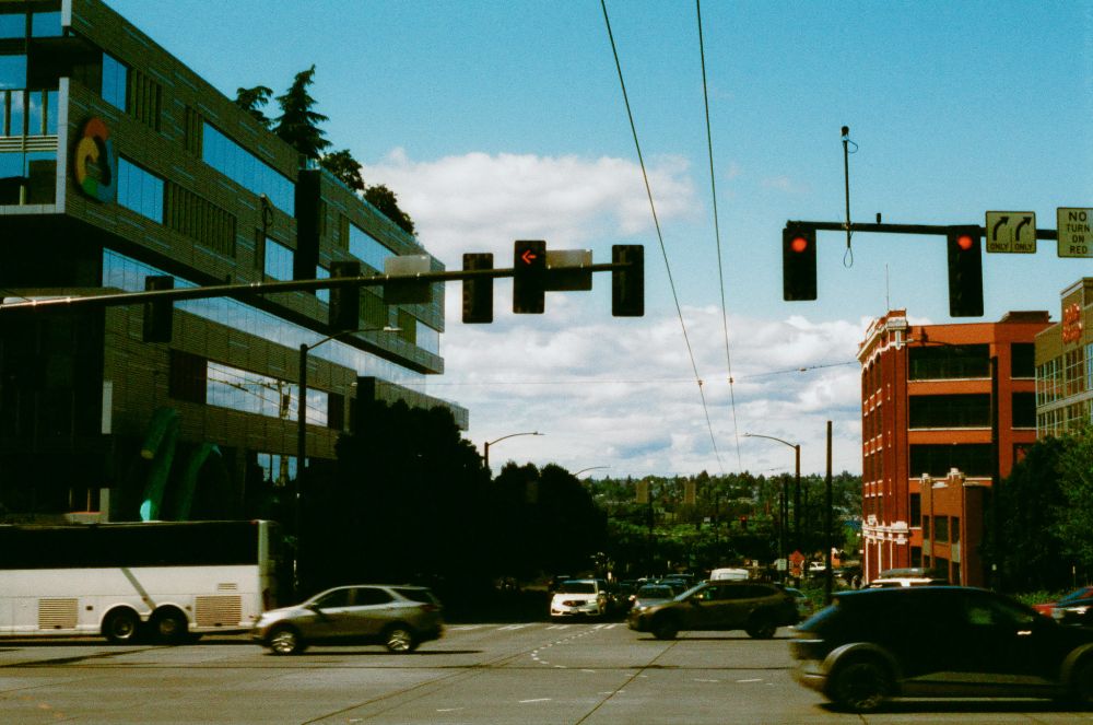 The Google building looms over a city street populated by cars zooming past on a sunny day. 