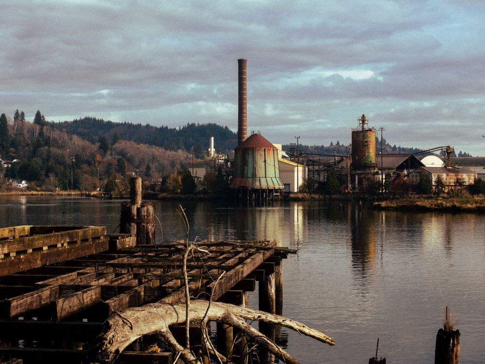 A rusted factory and a rotting pier on a sunny day. 
