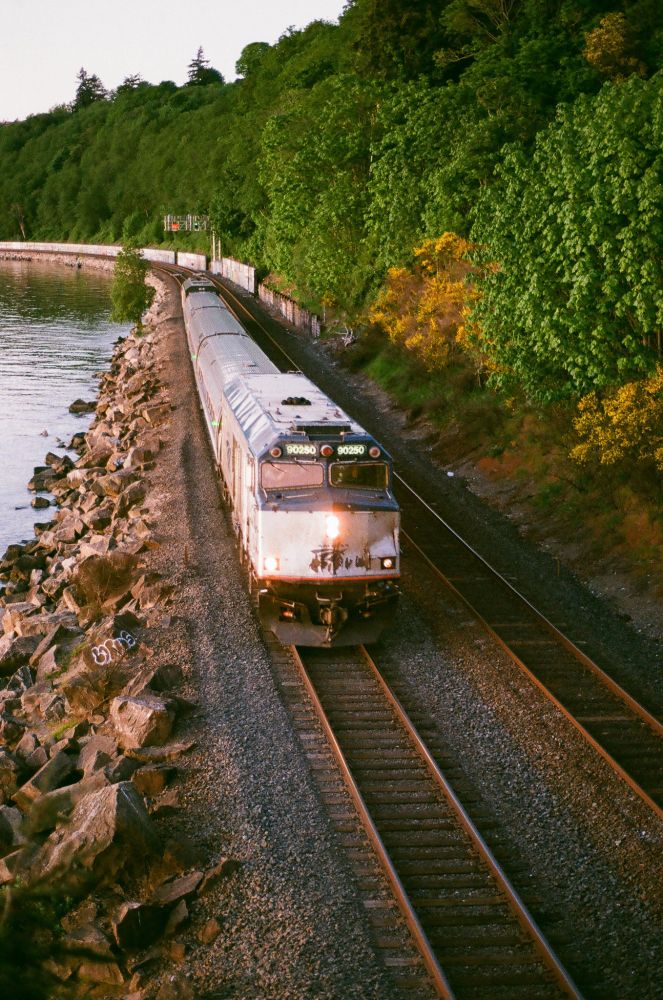a beat-to-shit Amtrak Cascades F40 cab car leads off the train as it whips down the shore of the Puget Sound at dusk.