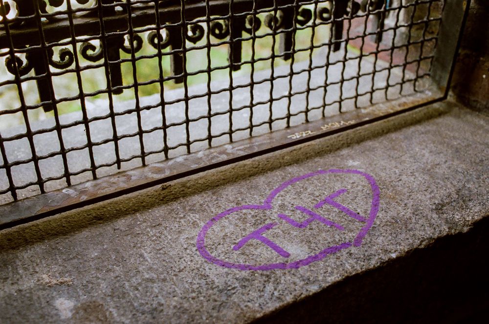 A small purple heart with T4T written inside it. Drawn on concrete behind a barred window. 