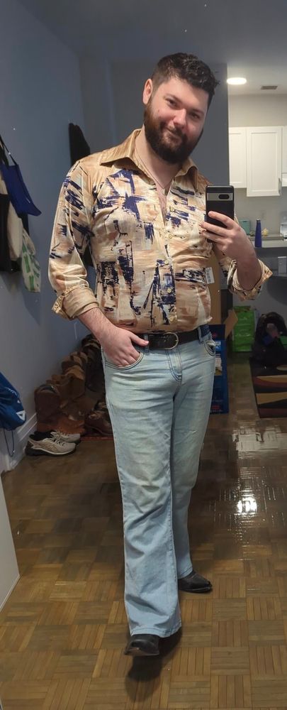 Man in disco shirt, lightwash flared jeans, and black cowboy boots