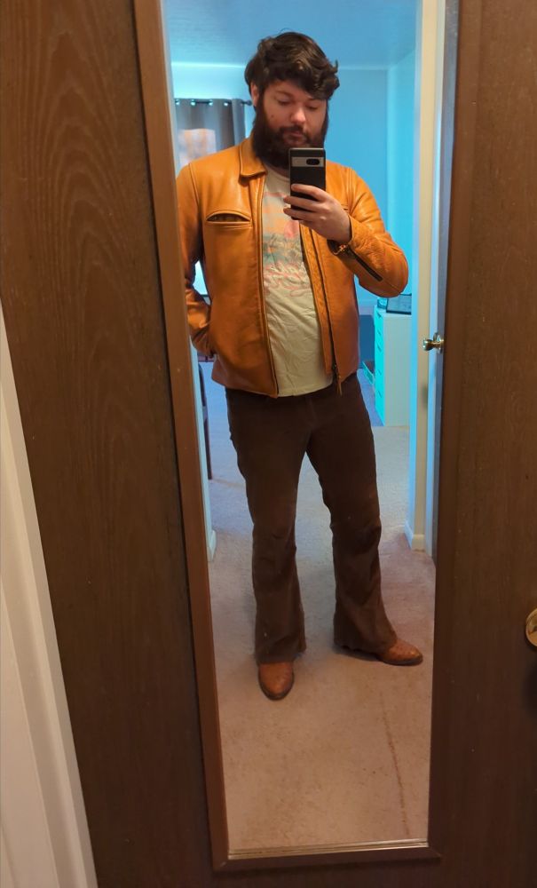 A man in an orange leather jacket, brown cord flares and ostrich cowboy boots