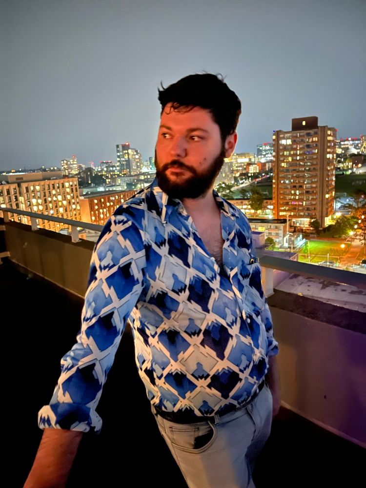 Same man in same outfit on a balcony with the Boston skyline in the background