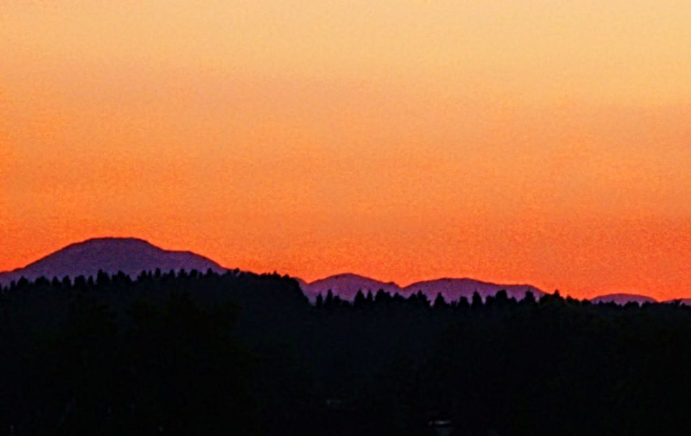 Sonnenaufgang im Juli, oranger Himmel, Jura in Lila und schwarzer Wald unten.