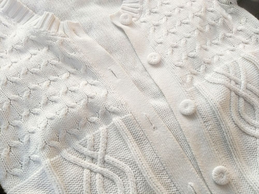 Knitted texture of a white jumper sweater, with cables, buttons and button holes