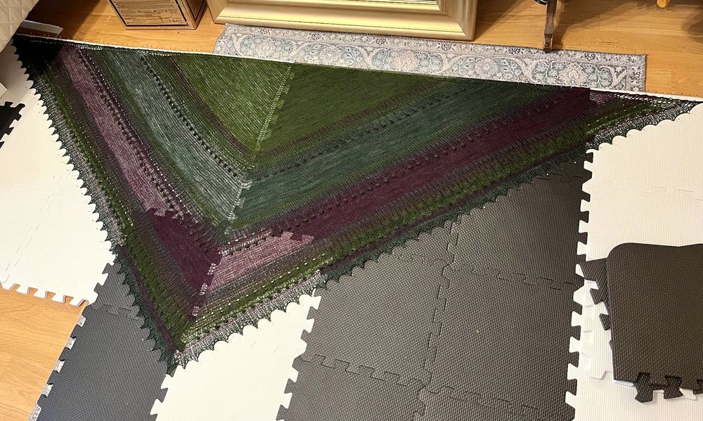 Purple and green knited shawl pinned to a black and white foam puzzle mat