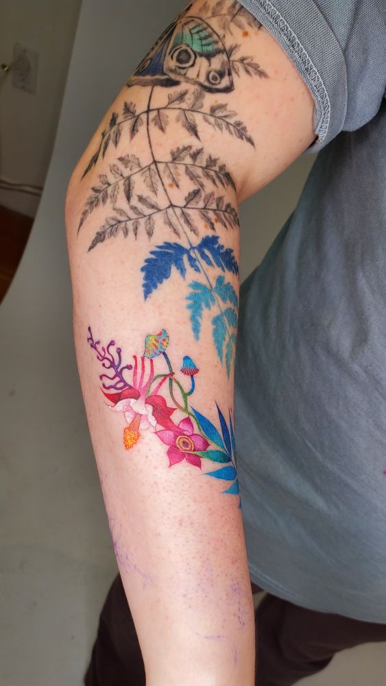 A brightly coloured tattoo with some red and pink flowers and some neon coloured mushrooms