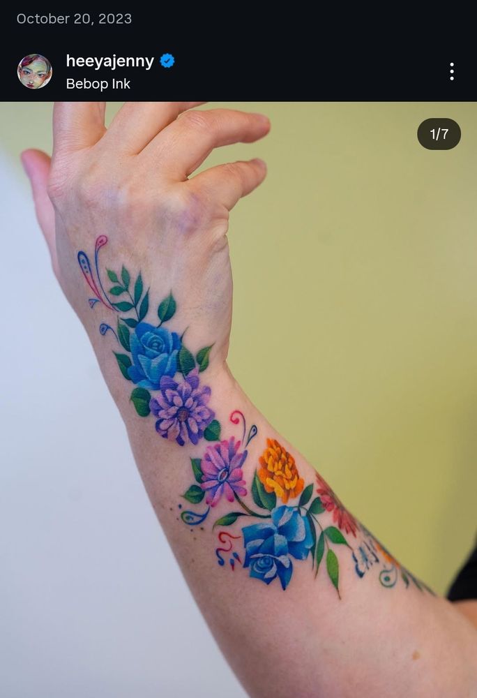 A flowery tattoo wrapping up a person's wrist and around their forearm. It's bright and colourful. Artist is heeyajenny on instagram