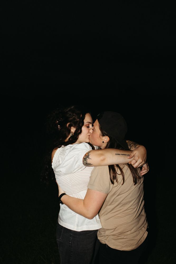 pic of me and my wife kissing, I’m on the left wearing a white top and jeans and I have my arms around Andi, who is on the left, wearing a tan t-shirt. The background is all black