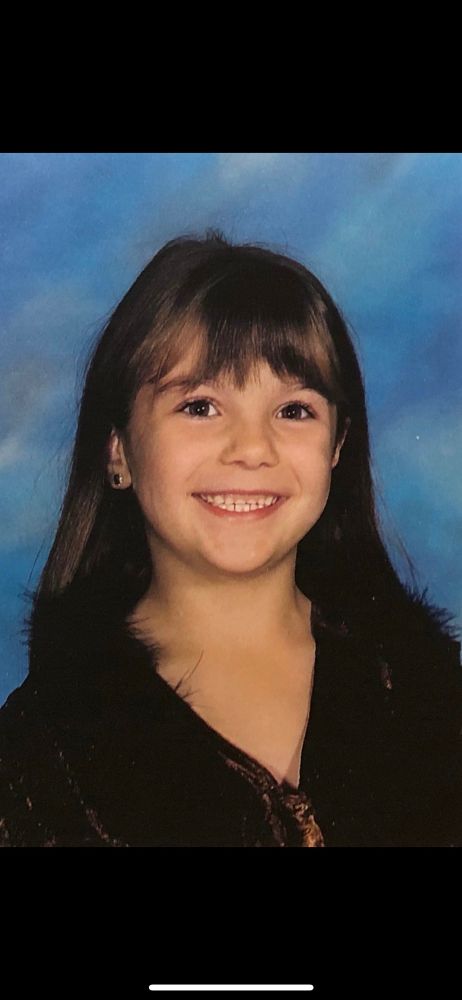 mar at (7?) years old with brown straight hair and bangs smiling with little teeny tiny baby teeth and wearing a brown velvet top with black feathers 