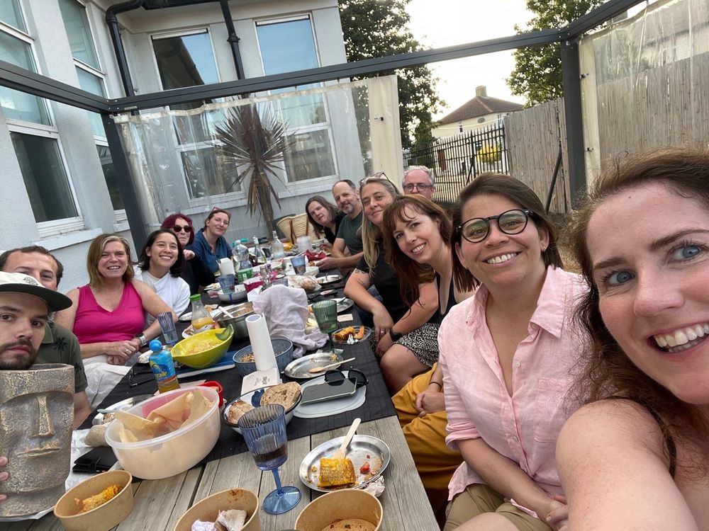 The Connecting Cabra committee - 12 smiling people sitting along a large picnic bench with food laid out on the table. 