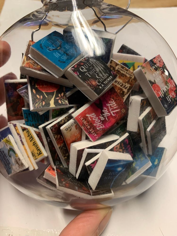 A clear Christmas ornament filled with dozens of tiny paper and foam books
