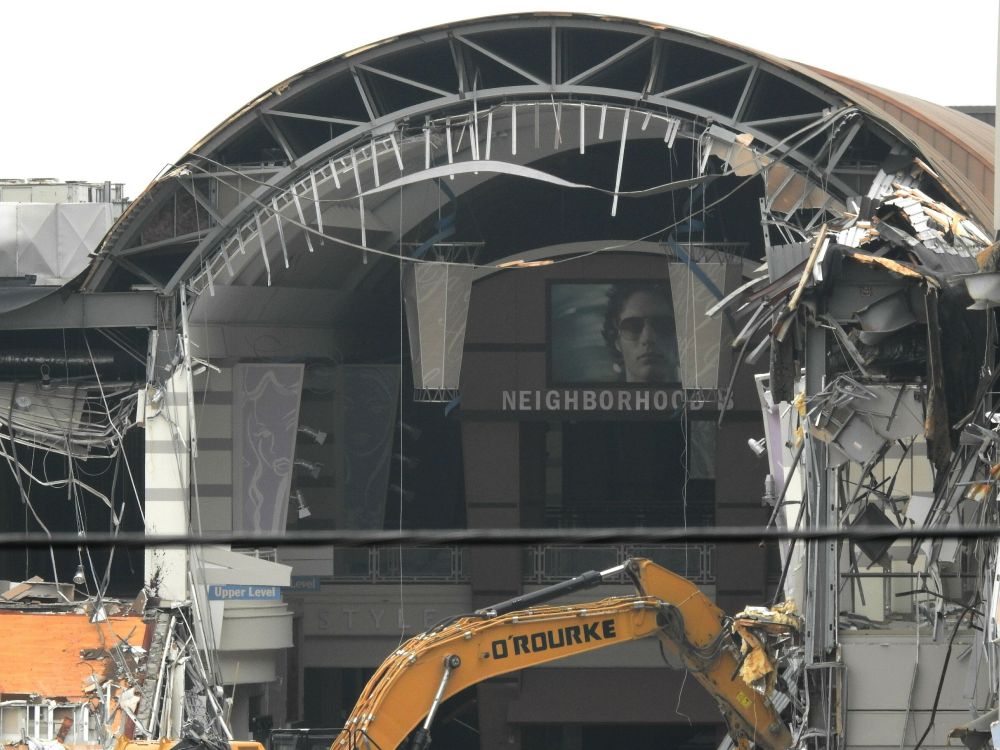 A shopping mall undergoing demolition, the tangled debris hanging off the main structure. 