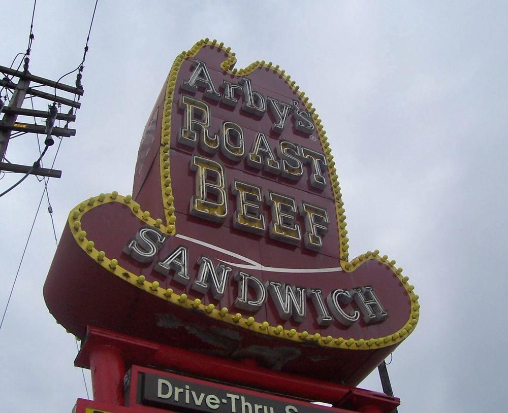 A close up of a 10 gallon hat sign covered in neon, with chaser bulbs lining the edge, advertising the Arby's chain of roast beef sandwich restaurants. 