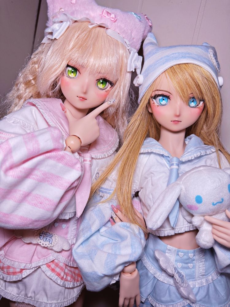 Two dolls. Dollfie dream Saber Extra, Nero, is wearing pink and showing off her new pink sparkly nails while holding Dollfie Dream Saber, Artoria’s arm. Artoria is dressed in a matching outfit to Nero’s but in blue.