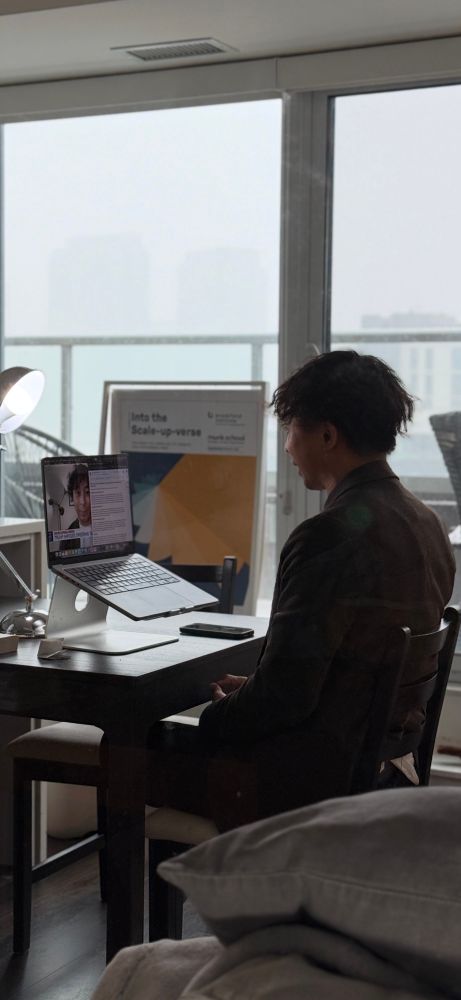 Photo of the back of Viet’s head in a chair doing a media interview. He is facing a laptop screen with the live TV feed of his face, alongside some speaking notes. It is snowing outside from the window.