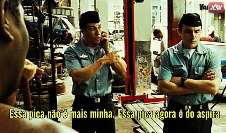 Cena de filme tropa de elite onde dois policiais fardados estão conversando em uma oficina de carros com o escrito em letras amarelas na parte debaixo da imagem da cena "essa pica não é mais minha. Essa pica agora é do aspira"
