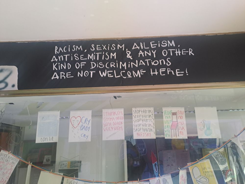 A sign above a store that says "Racism, sexism, aileism, antisemitism & any other discriminations are not welcome here!"