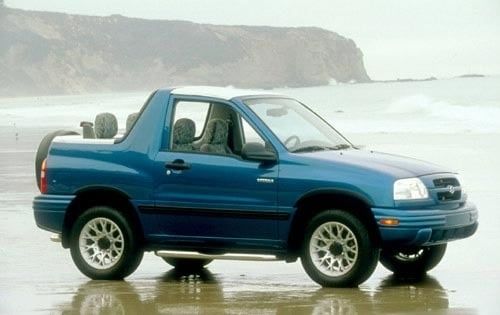 A blue Suzuki Vitara convertible parked on the beach on a foggy morning. It has it's roof down