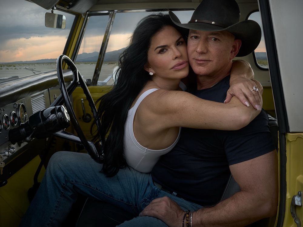 Jeff Bezos in cowboy cosplay with his Black Hole Sun video wife wrapping his arms around him. Looks like they’re in a vehicle on a savannah, implicitly having just murderer a big game animal. 