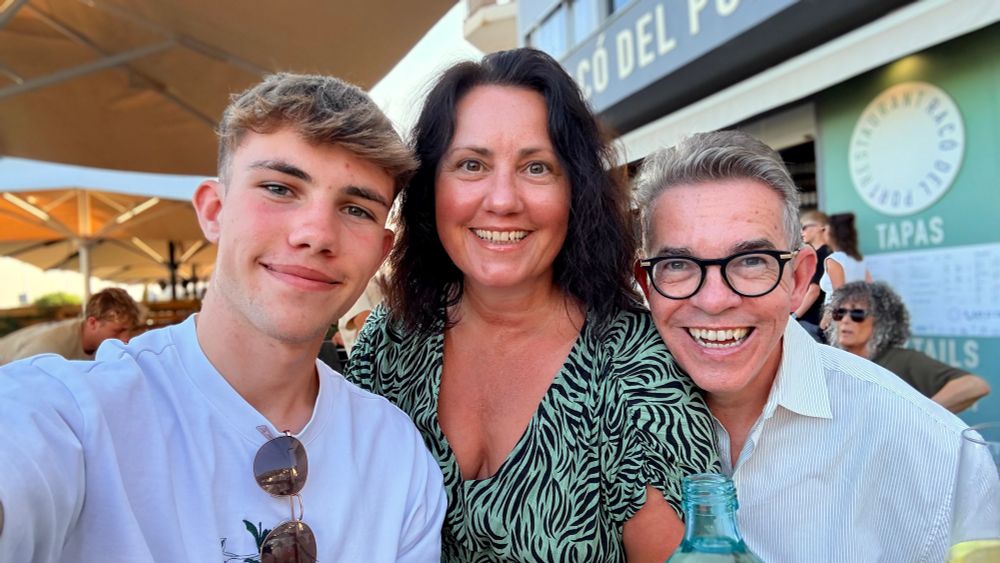 Family selfie at a restaurant in Catalunya – A smiling family group photo taken outside a tapas restaurant. Brendan stands on the right with his wife in the centre and their teenage son on the left. They’re all enjoying a sunny evening out.