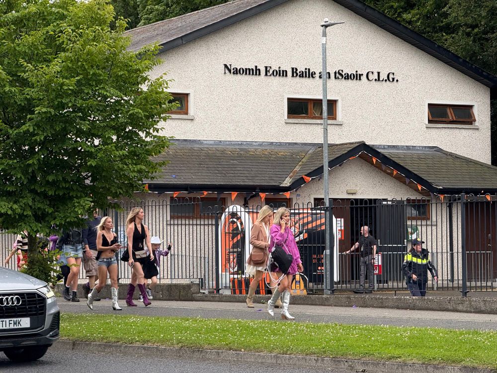 Groups of young people in festival-style outfits passing the front of Naomh Eoin Baile an tSaoir C.L.G. (St John’s GAA) clubhouse, en route to the Olivia Rodrigo concert