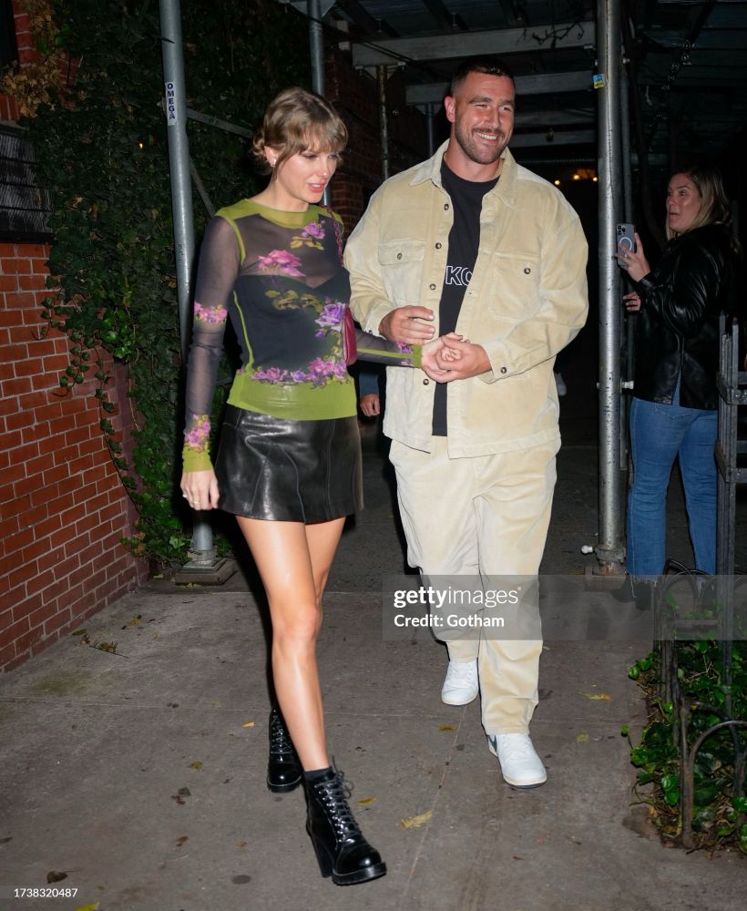 Taylor Swift and Travis Kelce exiting the Waverly Inn with a brick wall covered in ivy behind them. 