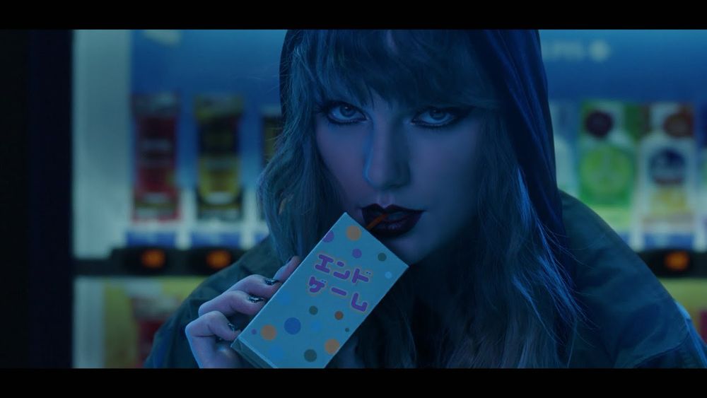 Taylor Swift dressed in a black hoodie sipping a juice box set in Tokyo for the endgame video. 