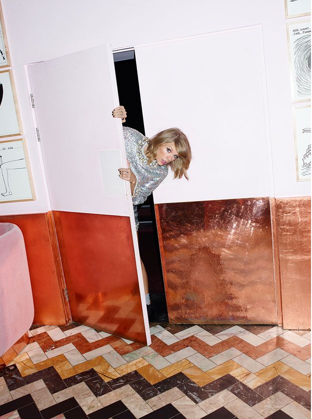 Taylor peeking out of a closet or restaurant swinging door into a room with autumn toned tiles. 