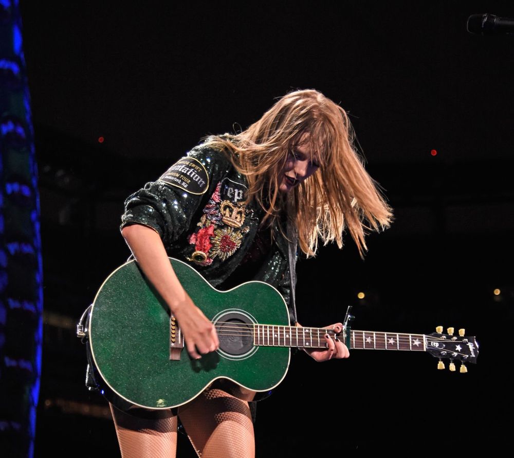 Taylor Swift playing her green guitar with wet hair. 