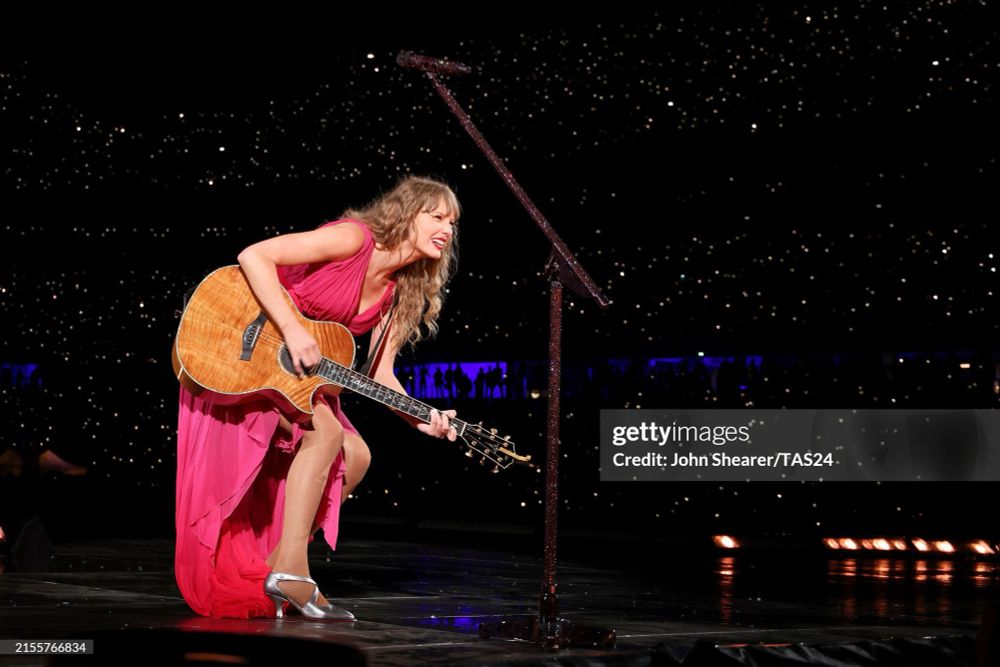 Taylor playing guitar in the pink surprise song dress. 