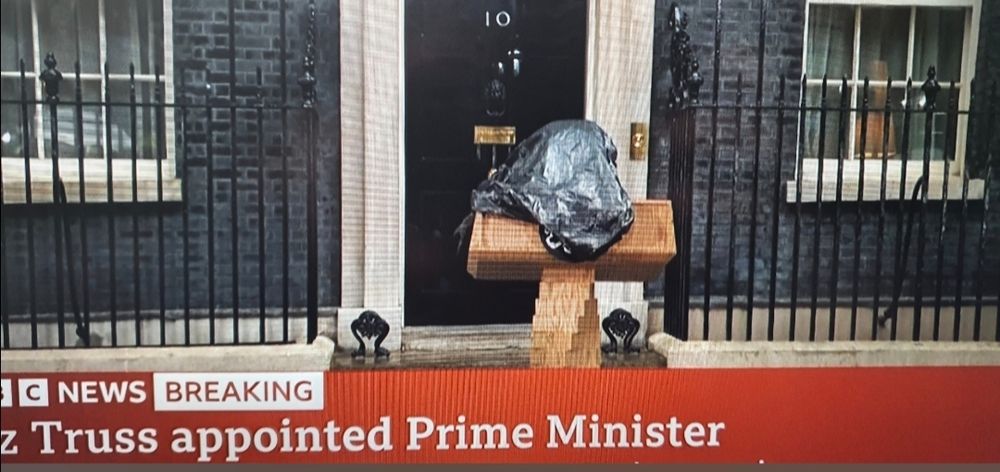 A picture of BBC News, the ticker reads "Liz Truss appointed Price minister. The image is of a podium outside downing Street, with a black bag draped over it in the rain.