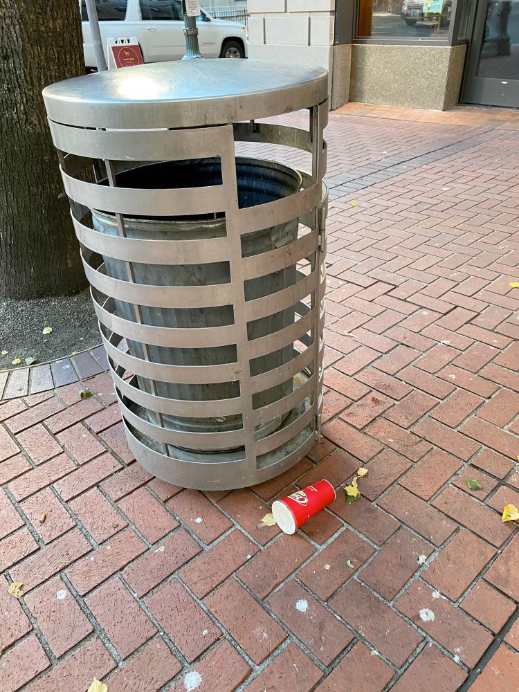 Image shows a single disposable cup on its side next to a trash can