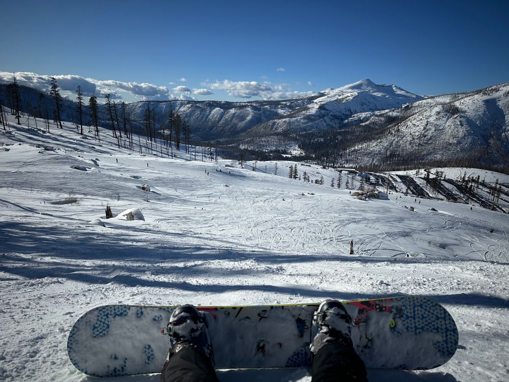 A view of snow-covered mountains (along with some sparse clouds in the distance) from Sierra at Tahoe, with a snowboard in the foreground.