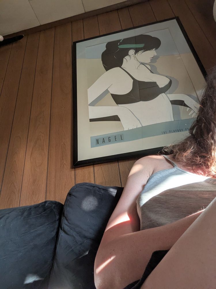 me sitting on the couch beneath a print of a Nagel girl.  she has big black hair and pale skin and big boobs and a lightening bolt earring