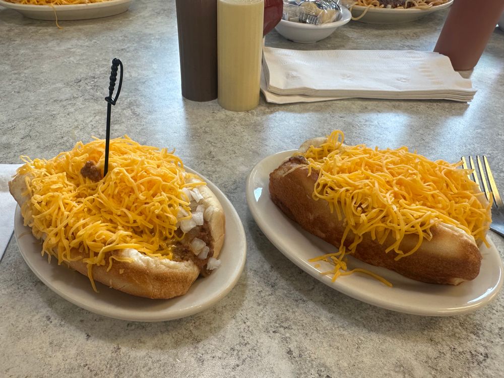 Two Skyline Chili coneys. Left one is chicken and right one is classic chili. The chicken one has a plastic sword in it. 